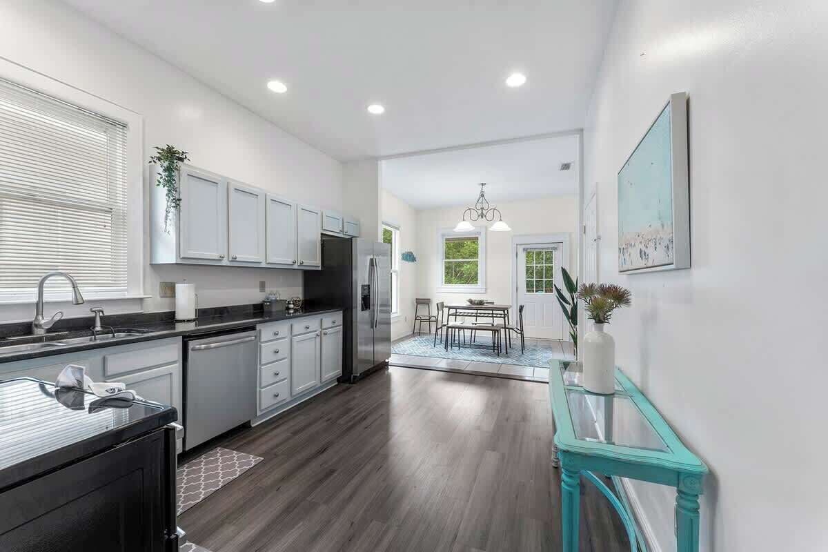 A modern kitchen with white cabinetry, a black countertop, and a dining area with a table and chairs.