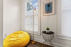 Ein Zimmer mit gelbem Sitzsack, einer Stehlampe, einem kleinen Tisch mit Pflanze und einem gerahmten Bild an der Wand.
