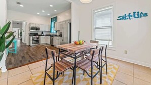 A modern kitchen with white cabinets, stainless steel appliances, and a dining area with a wooden table and chairs. - Historic Gem in Springfield - Grill, Private Deck (Jacksonville)