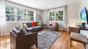 A spacious living room with a sofa, armchairs, a coffee table, and a TV. - Eclectic Escape #1 | Team Joseph Ellen (Jacksonville)
