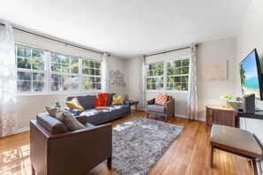 A spacious living room with a sofa, armchairs, a coffee table, and a TV. - Eclectic Escape #1 | Team Joseph Ellen (Jacksonville)