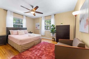 Ein Schlafzimmer mit Bett, Deckenventilator, Fenster, Pflanze und Nachttisch.