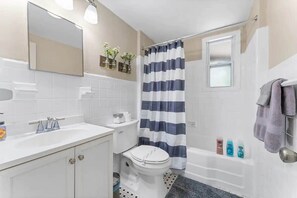 Ein Badezimmer mit Toilette, Waschbecken und Badewanne. Handtücher und Pflegeprodukte befinden sich an der Wand.