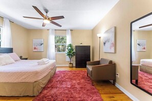 Une chambre à coucher avec un lit, une chaise, un ventilateur de plafond, une fenêtre et un miroir.