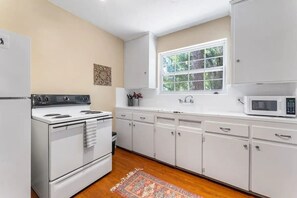 A kitchen with white cabinets, a stove, a microwave, and a window with a view of trees. - Eclectic Escape #1 | Team Joseph Ellen (Jacksonville)