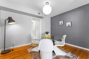 Ein modernes Wohnzimmer mit Glastisch, weißen Stühlen, einer Stehlampe und Deckenleuchte.