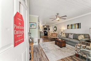 A living room with a sofa, coffee table, and a red sign on the wall. - The Poolside Cottage -Wifi,Pool (Jacksonville)