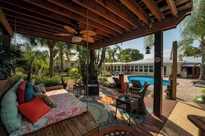 A covered outdoor seating area with a pool in the background.