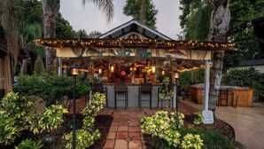 Un espace bar extérieur doté d’un coin salon abrité, entouré de plantes tropicales et bordé d’un chemin en pierre.