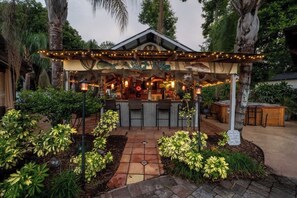 An outdoor bar area with a covered seating area, surrounded by tropical plants and a stone pathway. - The Poolside Cottage -Wifi,Pool (Jacksonville)