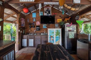 A rustic kitchen with wooden cabinets, a bar area, and a TV mounted on the wall. - The Poolside Cottage -Wifi,Pool (Jacksonville)
