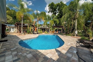 A swimming pool with a stone patio, surrounded by palm trees and a gazebo.