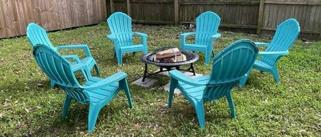 Un giardino retrostante con un braciere e sei poltrone Adirondack turchesi disposte attorno.