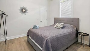 A bedroom with a bed, a ceiling fan, a window with blinds, a wall-mounted light fixture, and a small bedside table. - Historic bungalow - Wifi, Yard, Cozy (Jacksonville)