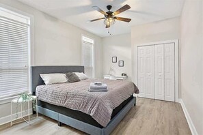 Un dormitorio con cama, ventilador de techo, paredes blancas y una puerta.