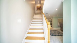 A staircase with wooden steps and a white railing, leading to a room with a patterned rug and a framed picture on the wall. - "Sea Grape Villa" Pool/ Ping Pong, (Jacksonville Beach)