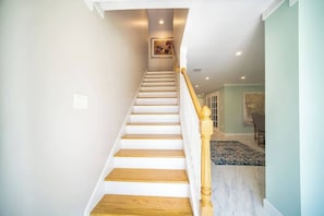 A staircase with wooden steps and a white railing, leading to a room with a patterned rug and a framed picture on the wall. - "Sea Grape Villa" Pool/ Ping Pong, (Jacksonville Beach)