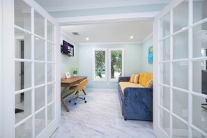 A room with a desk, office chair, sofa, and large windows. - "Sea Grape Villa" Pool/ Ping Pong, (Jacksonville Beach)