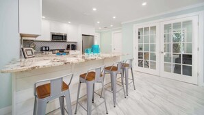 A modern kitchen with white cabinets, a marble countertop, and bar stools. - "Sea Grape Villa" Pool/ Ping Pong, (Jacksonville Beach)