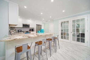 A modern kitchen with white cabinets, a marble countertop, and bar stools. - "Sea Grape Villa" Pool/ Ping Pong, (Jacksonville Beach)