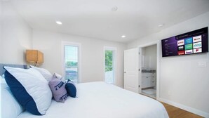 A bedroom with a bed, a TV mounted on the wall displaying various streaming services, and a door leading to a bathroom. - "Sea Grape Villa" Pool/ Ping Pong, (Jacksonville Beach)