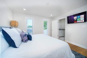 A bedroom with a bed, a TV mounted on the wall displaying various streaming services, and a door leading to a bathroom. - "Sea Grape Villa" Pool/ Ping Pong, (Jacksonville Beach)