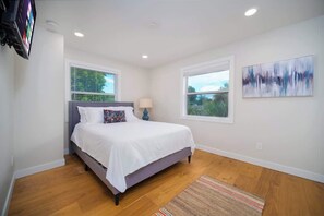 A bedroom with a bed, two windows, a painting, and a television. - "Sea Grape Villa" Pool/ Ping Pong, (Jacksonville Beach)