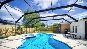 A covered swimming pool with a curved design, surrounded by a wooden fence and a patio area with a table and chairs. - "Sea Grape Villa" Pool/ Ping Pong, (Jacksonville Beach)