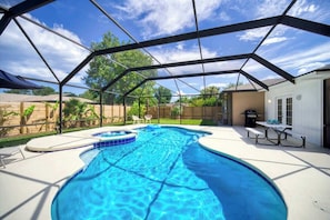 A covered swimming pool with a curved design, surrounded by a wooden fence and a patio area with a table and chairs. - "Sea Grape Villa" Pool/ Ping Pong, (Jacksonville Beach)