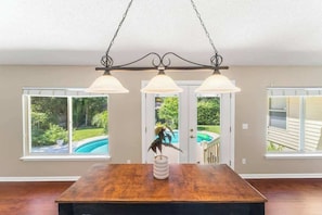 A dining area with a wooden table, three pendant lights, and a view of a swimming pool through a glass door. - Coastal Lane - Entire (Jacksonville)