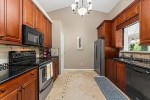 A kitchen with wooden cabinets, a black microwave, a stove, and a refrigerator. - Coastal Lane - Entire (Jacksonville)