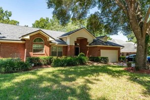 A residential house with a brick facade, a front yard with grass and shrubs, and a garage. - Coastal Lane - Entire (Jacksonville)