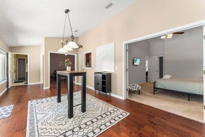 A spacious living area with hardwood flooring, a dining table, a sofa, and a bed in the adjacent room. - Coastal Lane - Entire (Jacksonville)