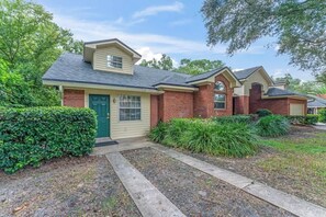 A residential building with a brick facade, a green door, and a small front yard with landscaping. - Coastal Lane - Entire (Jacksonville)