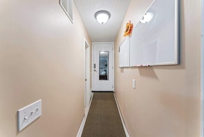A hallway with a carpeted floor, a white door, and a whiteboard on the wall. - Coastal Lane - Entire (Jacksonville)