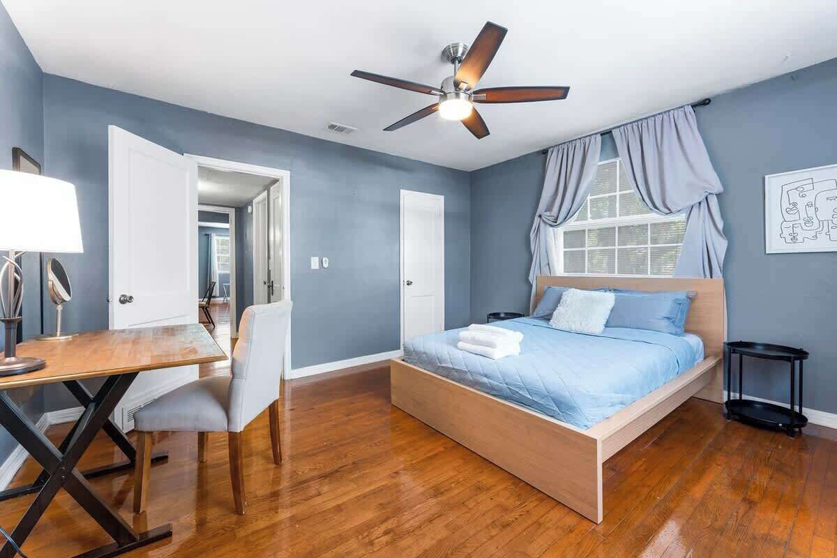A bedroom with a bed, a desk, a chair, a ceiling fan, and a window with curtains.