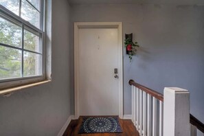 Ein Flur mit einer weißen Tür, einem Fenster, einem Holzgeländer und einer Fußmatte.