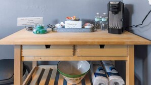 Une table en bois avec une machine à café, des bouteilles d’eau, un bol et un panneau.