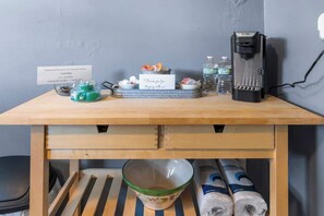 Ein Holztisch mit einer Kaffeemaschine, Wasserflaschen, einer Schüssel und einem Schild.