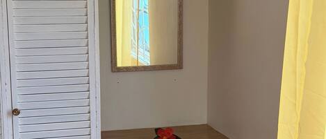 A room with a white door, a mirror above a wooden dresser, and a yellow curtain on the right.