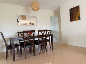 A dining area with a wooden table and chairs, a woven pendant light, a mirror, and a wall-mounted artwork.