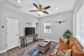 Un salon doté d’un ventilateur de plafond, d’un téléviseur à écran plat, d’une table basse en bois, d’un tapis à motifs, d’un canapé en cuir et d’une décoration murale représentant une tête de taureau.