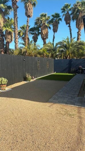 Un jardin avec un espace recouvert de gravier, une pelouse verdoyante et une clôture en bois.