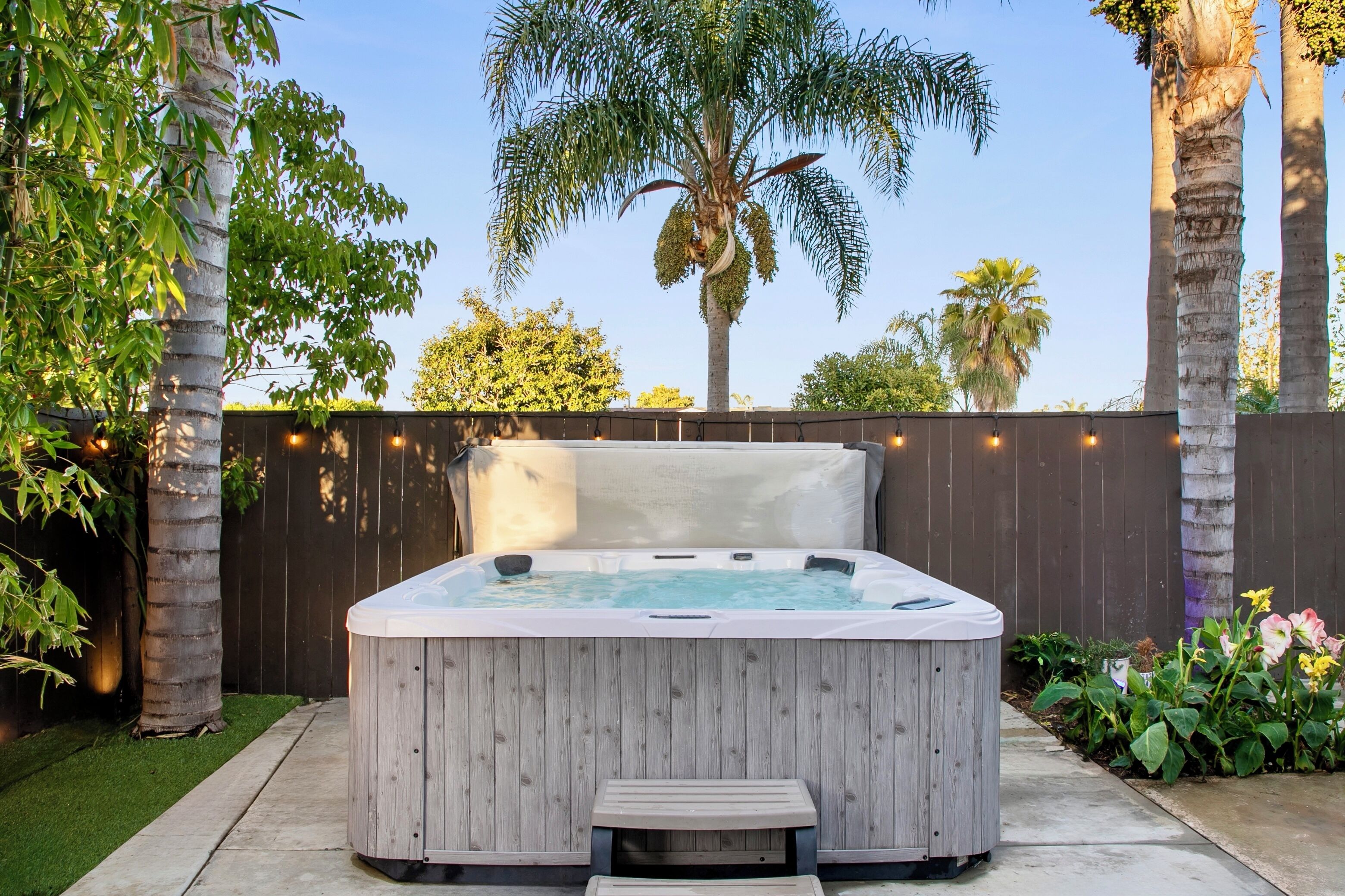 A hot tub with a wooden exterior, surrounded by a wooden fence and palm trees.