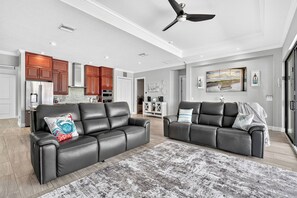 A spacious living room with two leather sofas, a patterned rug, and a ceiling fan. - VRCC Villa Penny River (Cape Coral)