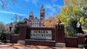 Ein Backstein-Eingang mit einem Schild, auf dem 'AUBURN UNIVERSITY ESTABLISHED 1856' steht, und ein Glockenturm im Hintergrund.