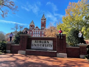 Ein Backstein-Eingang mit einem Schild, auf dem 'AUBURN UNIVERSITY ESTABLISHED 1856' steht, und ein Glockenturm im Hintergrund.