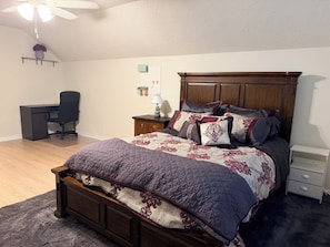Quarto com cama de madeira, escrivaninha, cadeira e mesa de cabeceira.