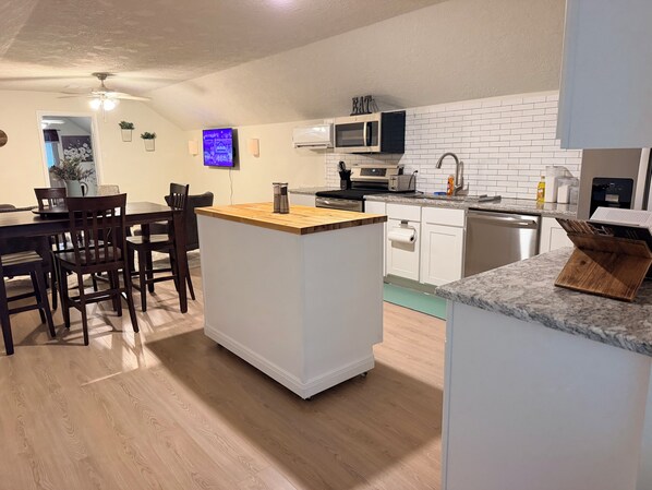 A modern kitchen with white cabinetry, a wooden island, and a dining area with dark wooden chairs. - Furnished Apartment l League City l Business & Medical Travelers (Dickinson)