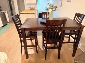 A dining table with four wooden chairs, a vase with flowers, and a kitchen in the background. - Furnished Apartment l League City l Business & Medical Travelers (Dickinson)
